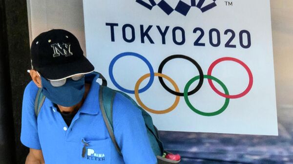 Прохожий возле баннера с символикой Олимпийских игр в Токио