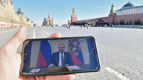 Житель Москвы смотрит на Красной площади со смартфона трансляцию обращения президента России Владимира Путина к гражданам из-за ситуации с коронавирусом Житель Москвы смотрит на Красной площади со смартфона трансляцию обращения президента России Владимира Путина к гражданам из-за ситуации с коронавирусом