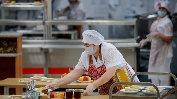 Работница школьной столовой разносит тарелки с едой Работница школьной столовой разносит тарелки с едой