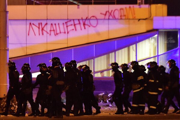 Сотрудники правоохранительных органов проходят мимо здания с надписью Лукашенко уходи! во время массовой акции протеста после президентских выборов в Минске, Беларусь Сотрудники правоохранительных органов проходят мимо здания с надписью Лукашенко уходи! во время массовой акции протеста после президентских выборов в Минске, Беларусь