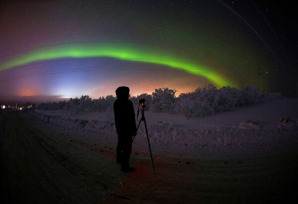 Мужчина фотографирует северное сияние на трассе Серебрянка в Мурманской области Мужчина фотографирует северное сияние на трассе Серебрянка в Мурманской области