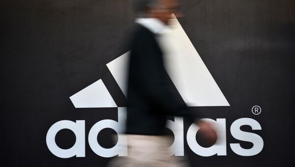 Человек проходит мимо логотипа Adidas. Архивное фото Человек проходит мимо логотипа Adidas. Архивное фото