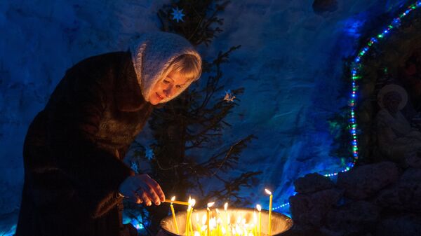 Женщина зажигает свечу в снежном Рождественском вертепе во время праздничной Рождественской службы в Богоявленском соборе в Томске Женщина зажигает свечу в снежном Рождественском вертепе во время праздничной Рождественской службы в Богоявленском соборе в Томске