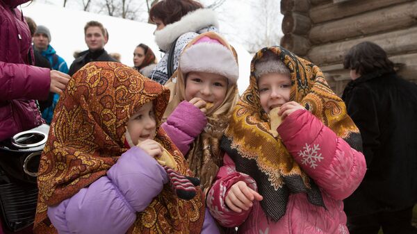 Дети едят блины во время праздничных гуляний на Масленицу