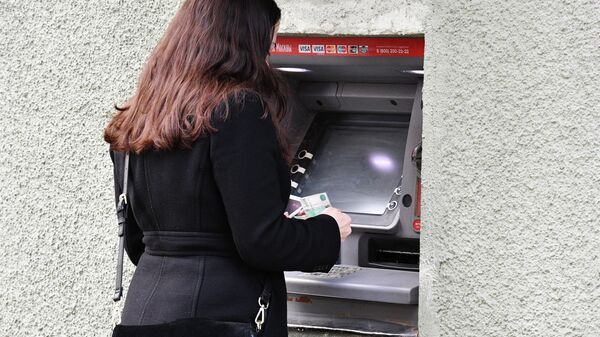 Девушка снимает наличные в банкомате на улице Москвы